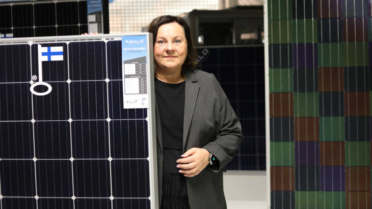 Solar Finland Oyn toimitusjohtaja Anu Areva seisoo aurinkopaneelien kanssa yrityksen tehtaan tiloissa.