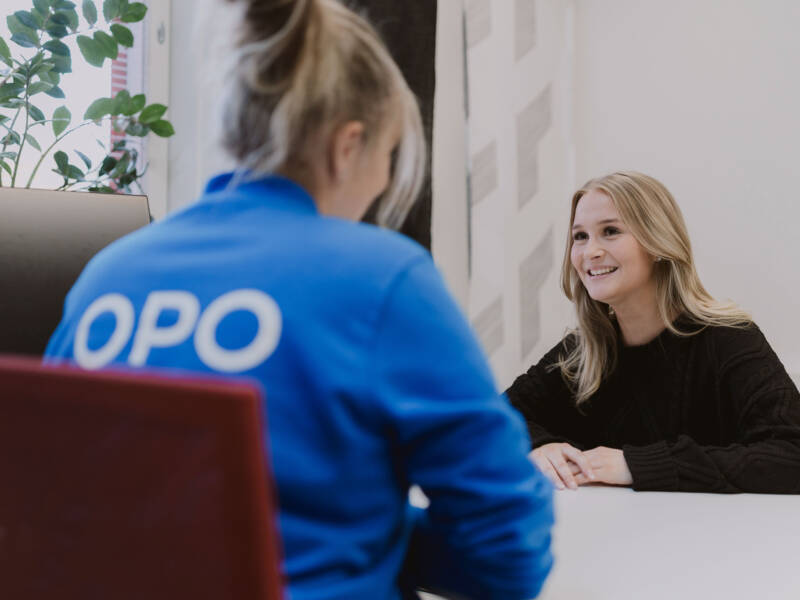 Iloinen nuori naisopiskelija keskustelee opinto-ohjaajan kanssa toimistossa