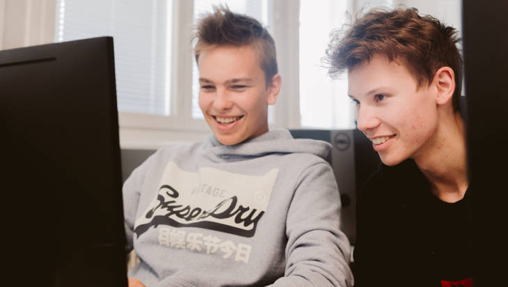 Kaksi tieto- ja viestintätekniikan opiskelijaa istuu tietokoneen ääressä hymyillen.