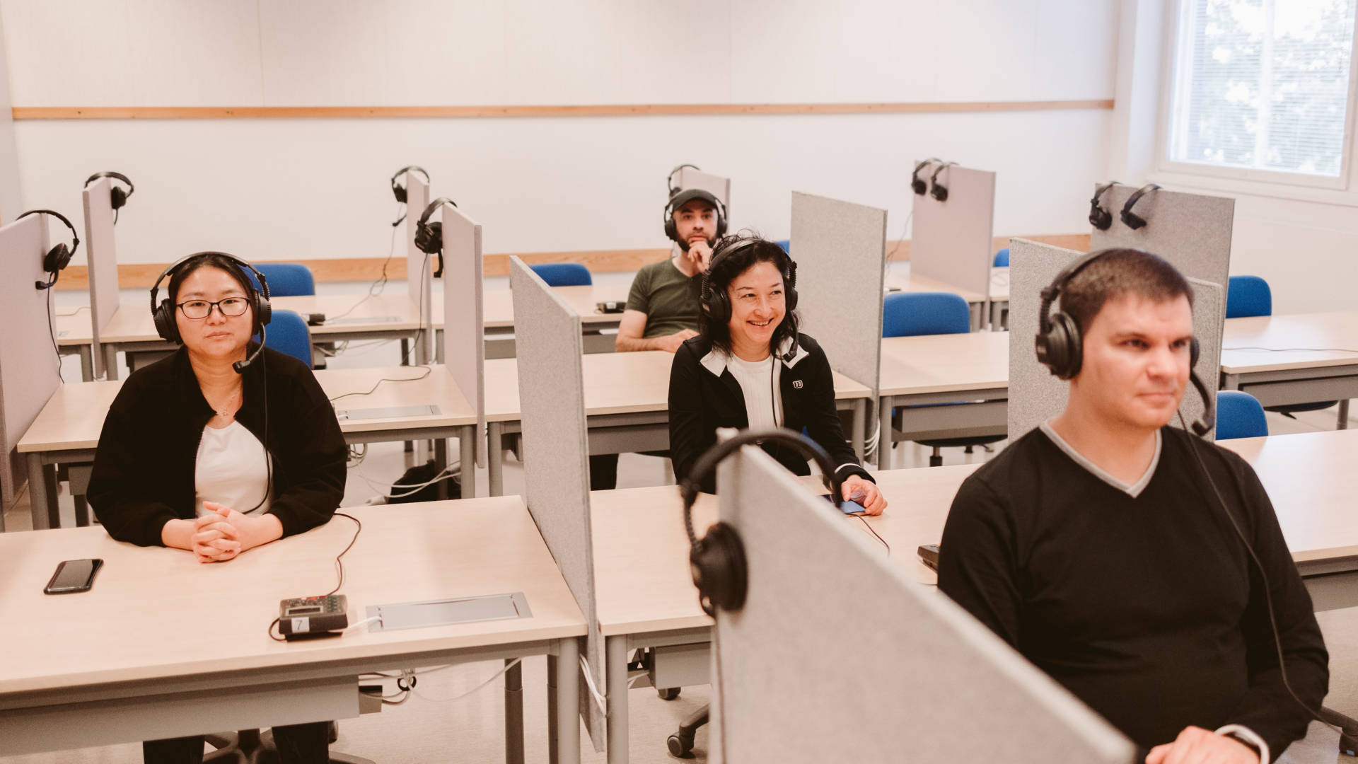 Neljä kansainvälistä opiskelijaa istuu kieliluokassa kuulokkeet päässä ja katsoo luokkahuoneen etuosaan.