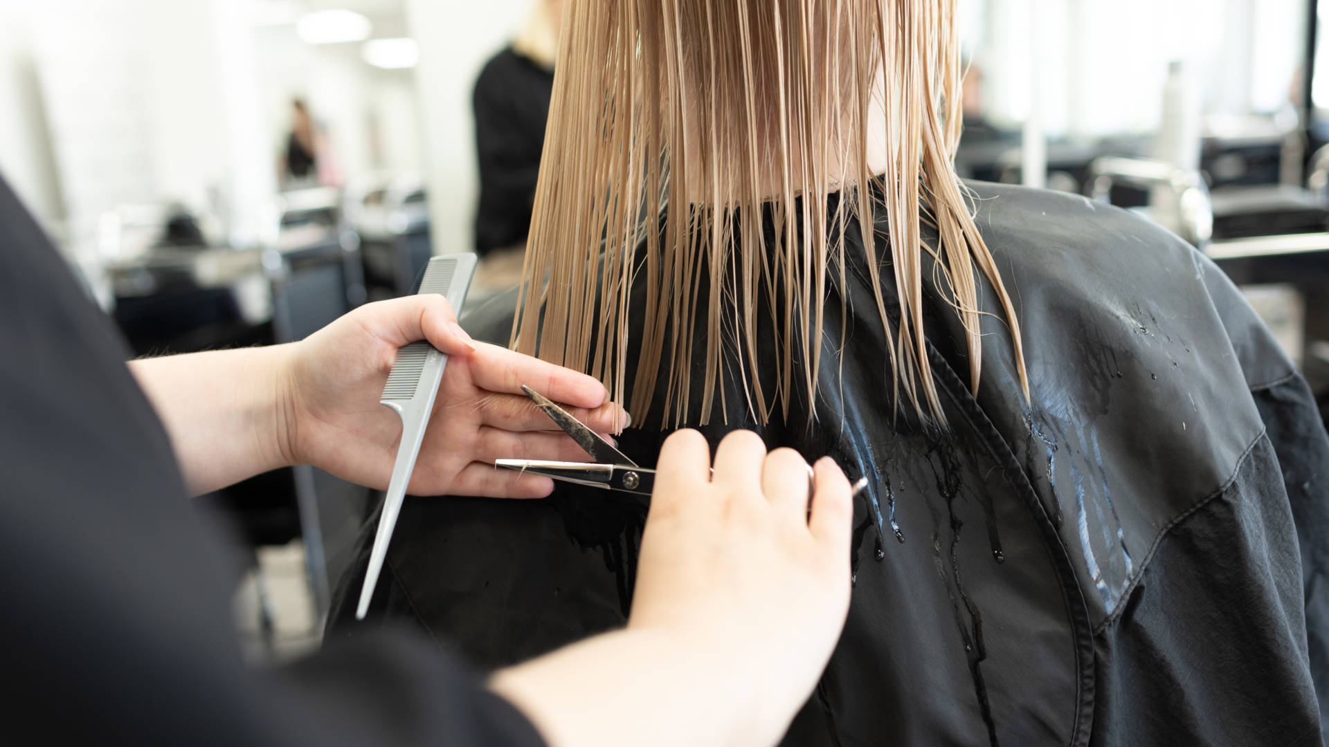 Salon seudun ammattiopiston parturikampaamo AmiStylessä opiskelija tasoittaa asiakkaan hiuksia.