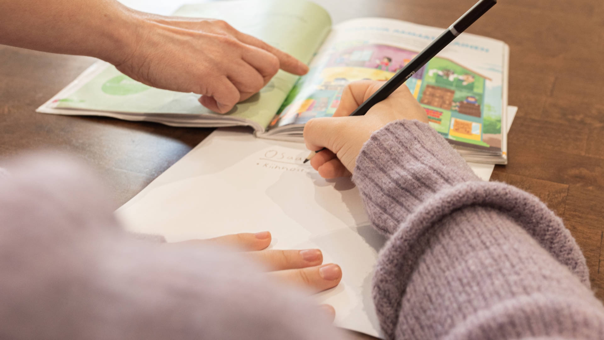 Aikuinen osoittaa oppikirjasta lapselle oikean kohdan ja lapsi kirjoittaa oppimansa.
