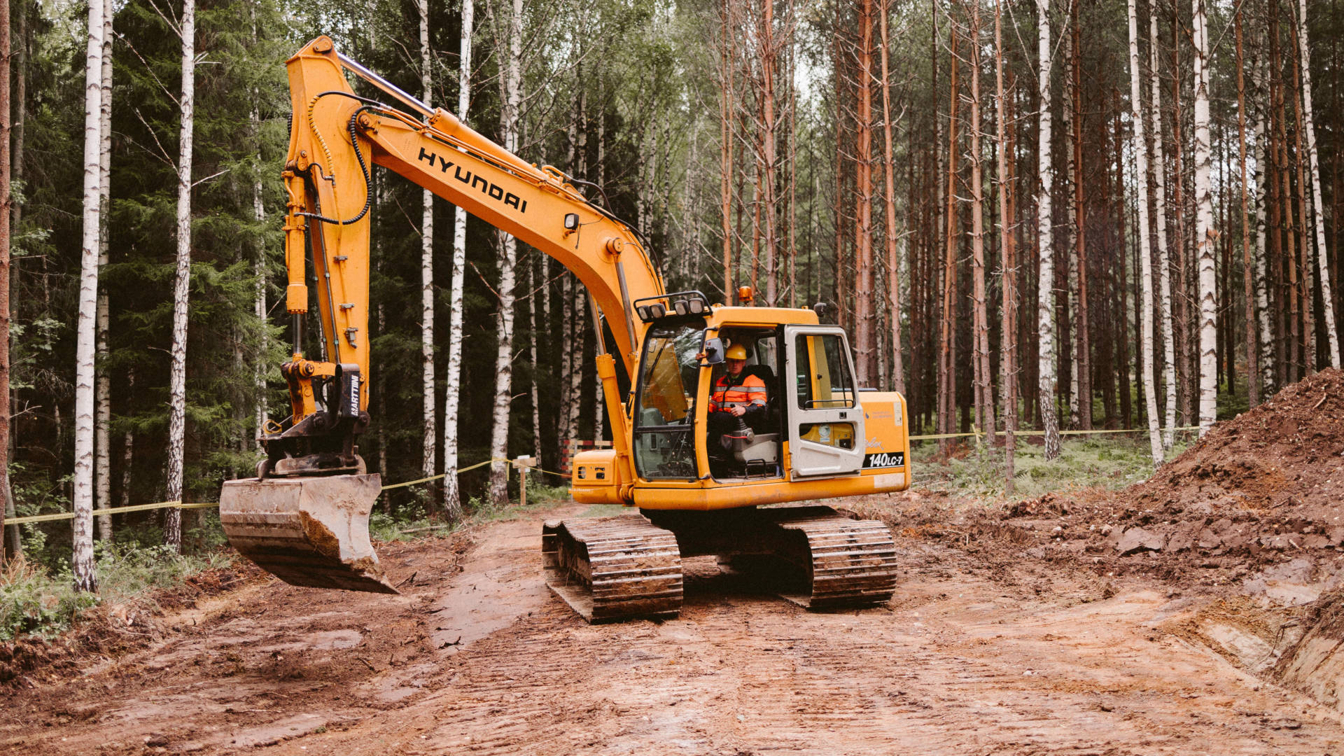 Maarakennusalan opiskelija harjoittelee keltaisen kaivinkoneen kääntymistä metsässä.