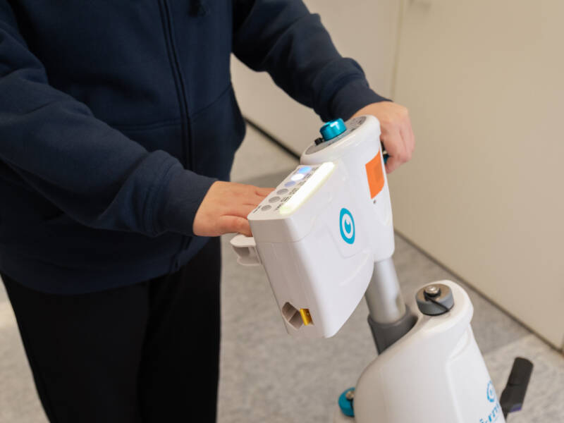 Opiskelija ohjaa lattianpesurobottia rakennuksen käytävällä.