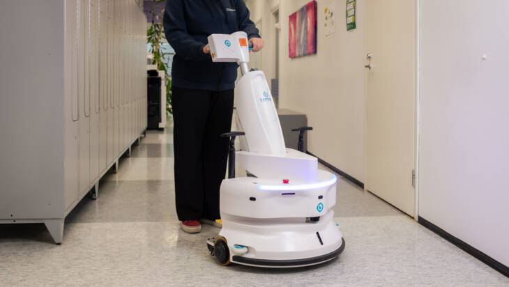 Opiskelija ohjaa lattianpesurobottia oppilaitoksen sisäkäytävässä.